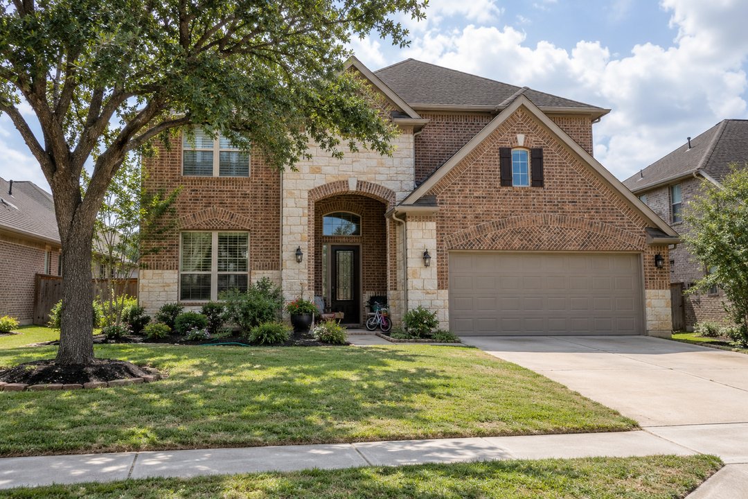 A two-story brick and stone home with a tree in the front yard